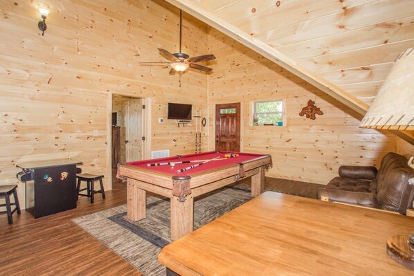 A wooden interior with a pool table, a sofa, and a ceiling fan.