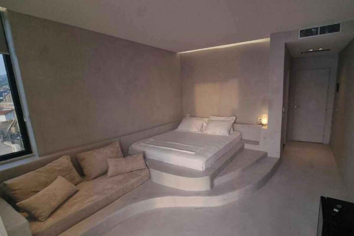 A modern bedroom with a bed, a sofa, and a TV.