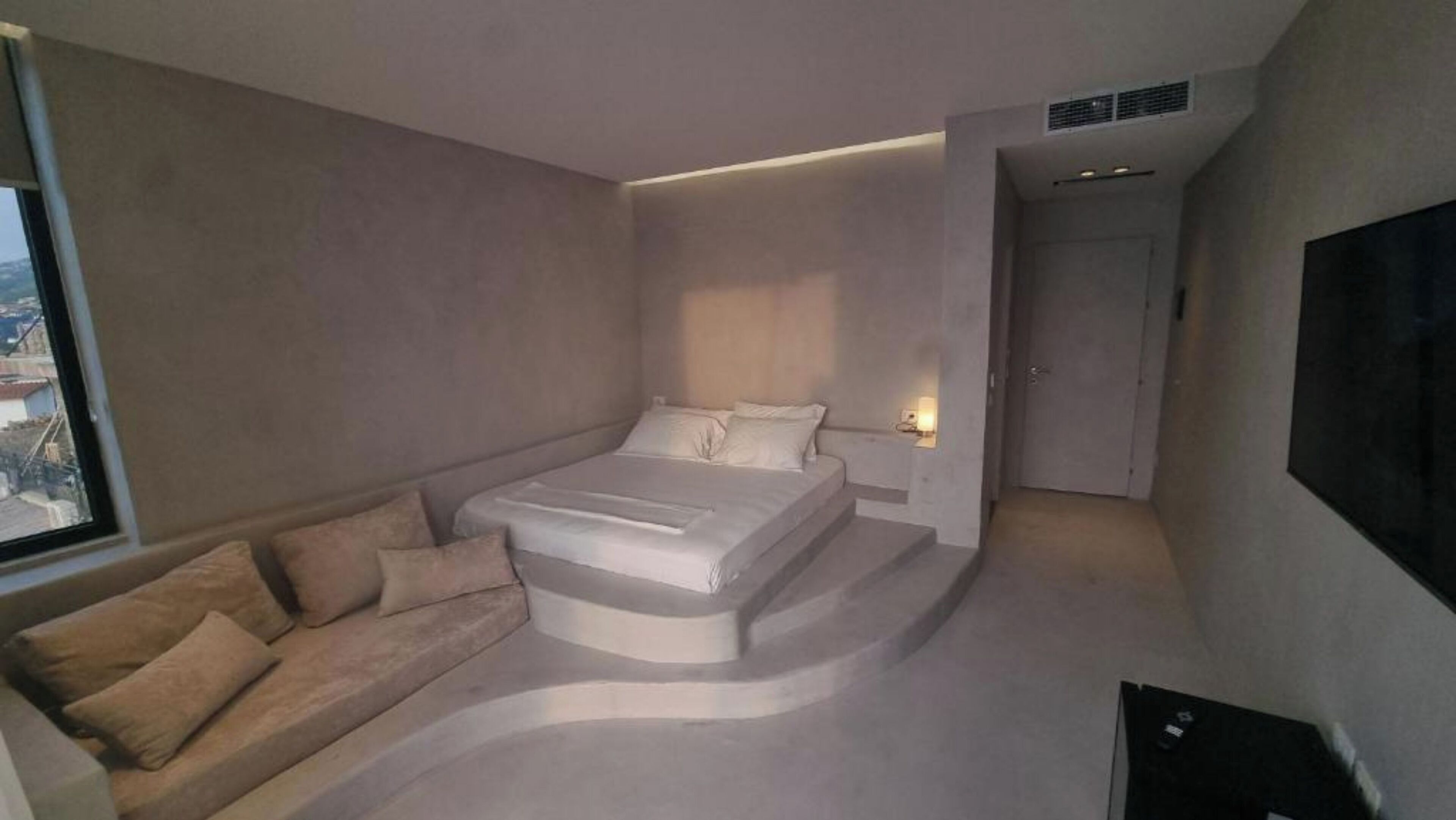 A modern bedroom with a bed, a sofa, and a TV.