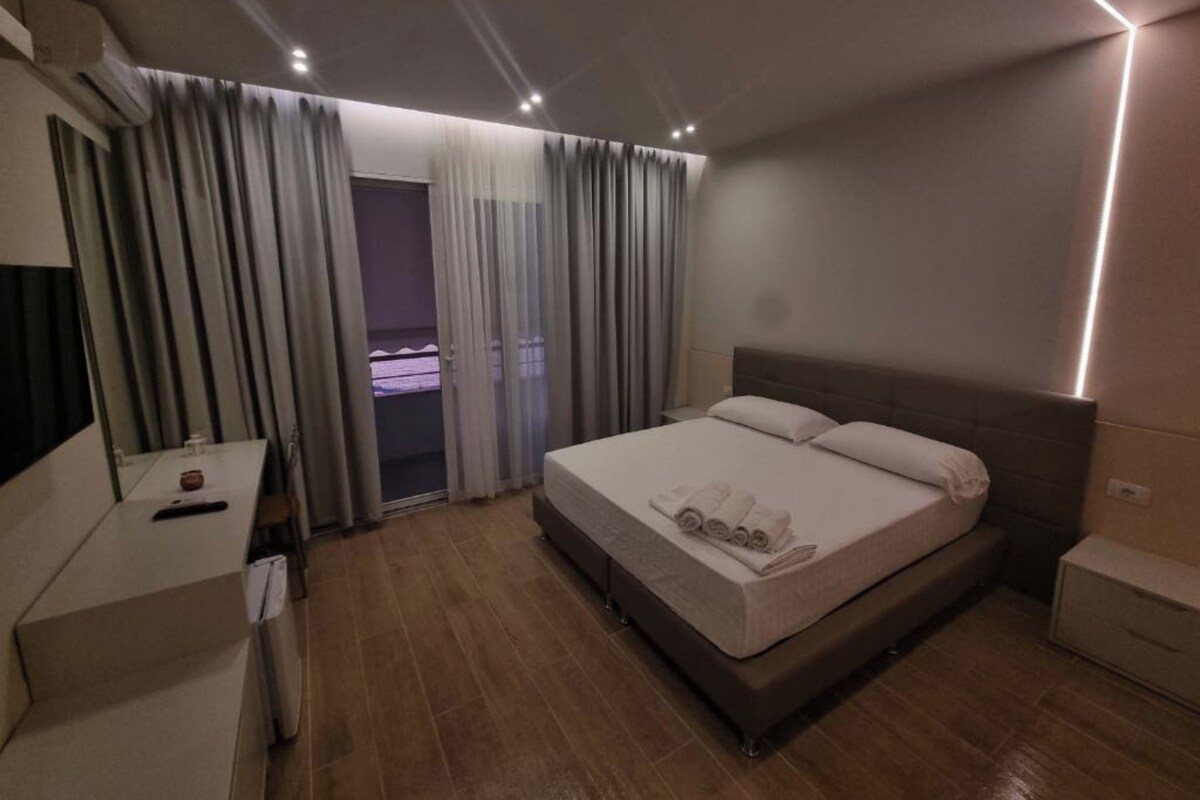 A hotel room with a bed, a desk, a chair, a wardrobe, and a window with curtains.