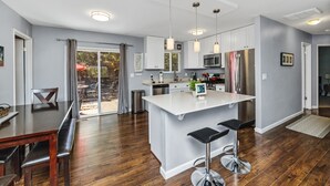 A modern kitchen with white cabinetry, stainless steel appliances, and a central island with bar stools. - REMODELED 3Bd/2Bth TreeTop House -> Downtown Location w/ Views & 5-STAR REVIEWS! (Prescott)