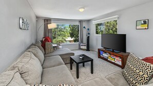 A living room with a sofa, a coffee table, a TV, and a window with curtains. - REMODELED 3Bd/2Bth TreeTop House -> Downtown Location w/ Views & 5-STAR REVIEWS! (Prescott)