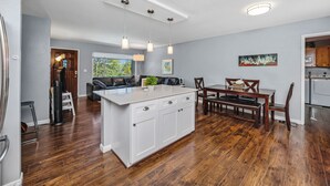 A modern kitchen with a central island, pendant lighting, and a dining area with a wooden table and chairs. - REMODELED 3Bd/2Bth TreeTop House -> Downtown Location w/ Views & 5-STAR REVIEWS! (Prescott)