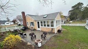 Una casa con porche cubierto, mobiliario exterior y un hogar para la chimenea.
