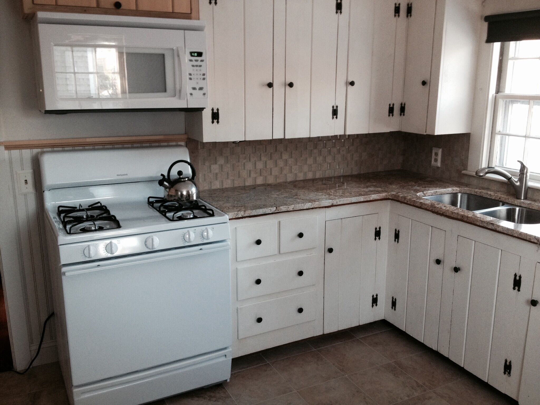 A kitchen with white cabinets, a stove, a microwave, and a sink.