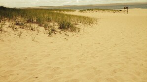 Una playa arenosa con dunas y un cartel a lo lejos.