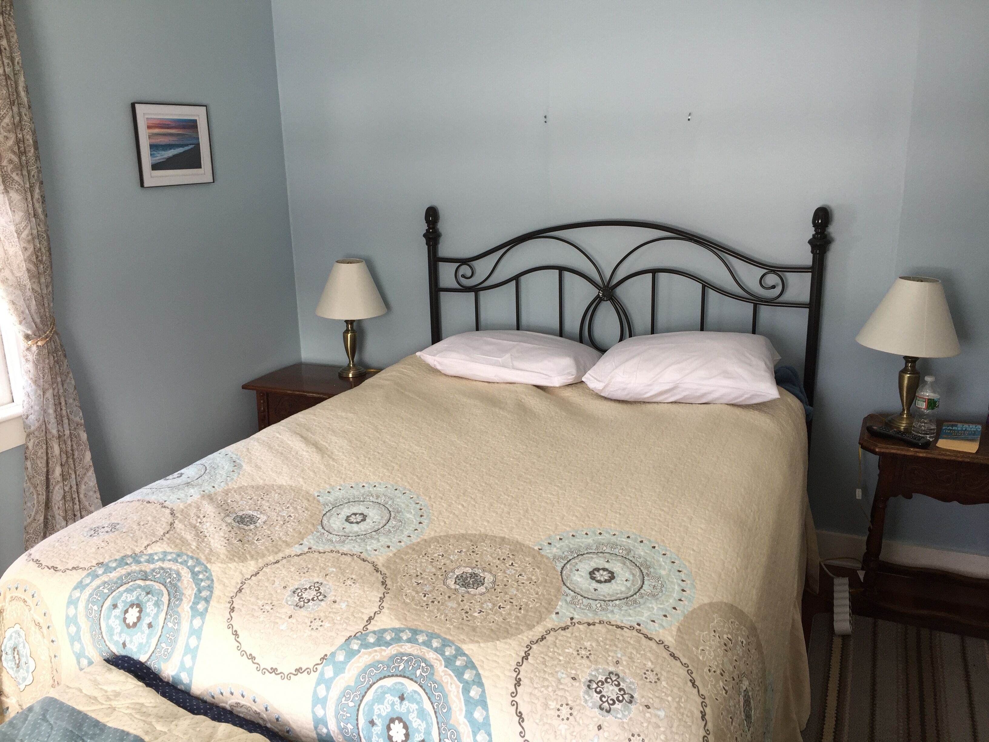 A neatly made bed with a patterned bedspread, two bedside lamps, and a framed picture on the wall.