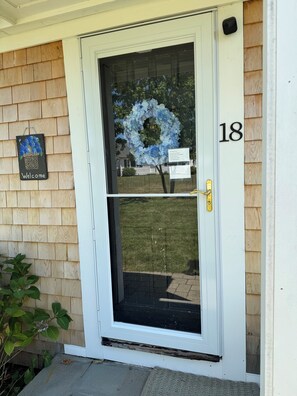 A white door with a glass panel, a number '18' above it, and a welcome sign with a floral design.