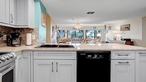 Une cuisine avec des meubles blancs, un lave-vaisselle noir, une cuisinière et un plan de travail en granit.