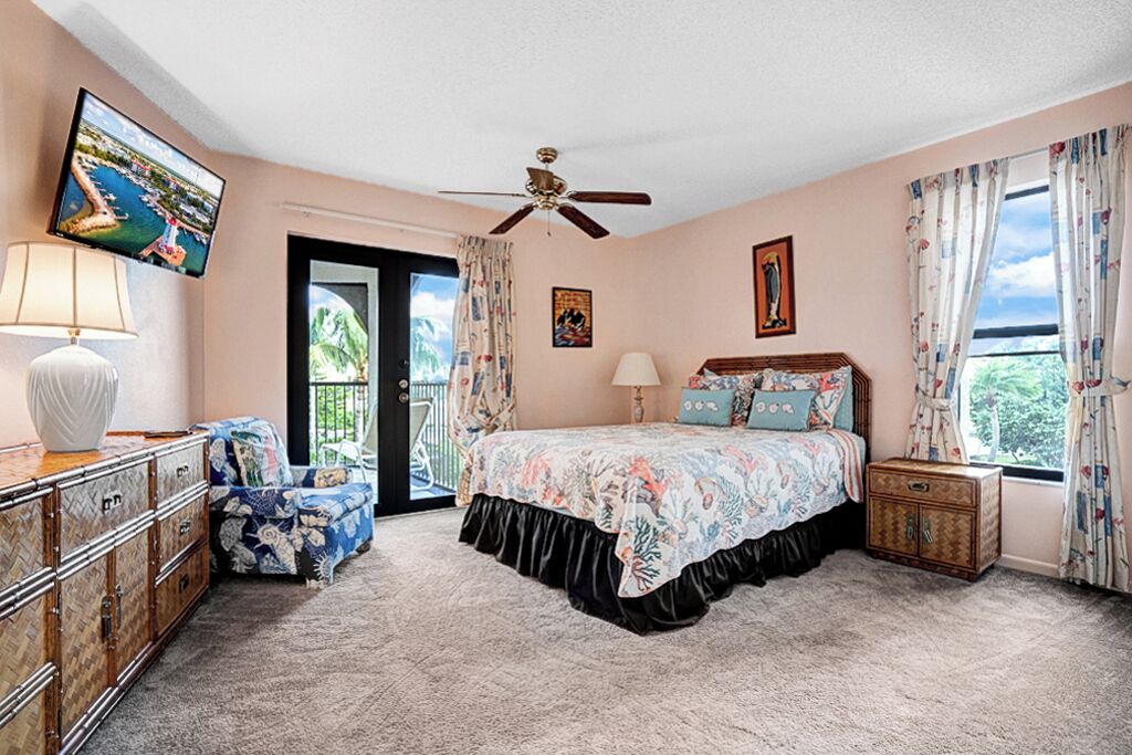 Un dormitorio con cama, cómoda, televisor, ventilador de techo y ventana con cortinas.