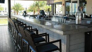 Un espace bar doté d’un long comptoir, de nombreux tabourets et offrant une vue sur les palmiers à l’extérieur.