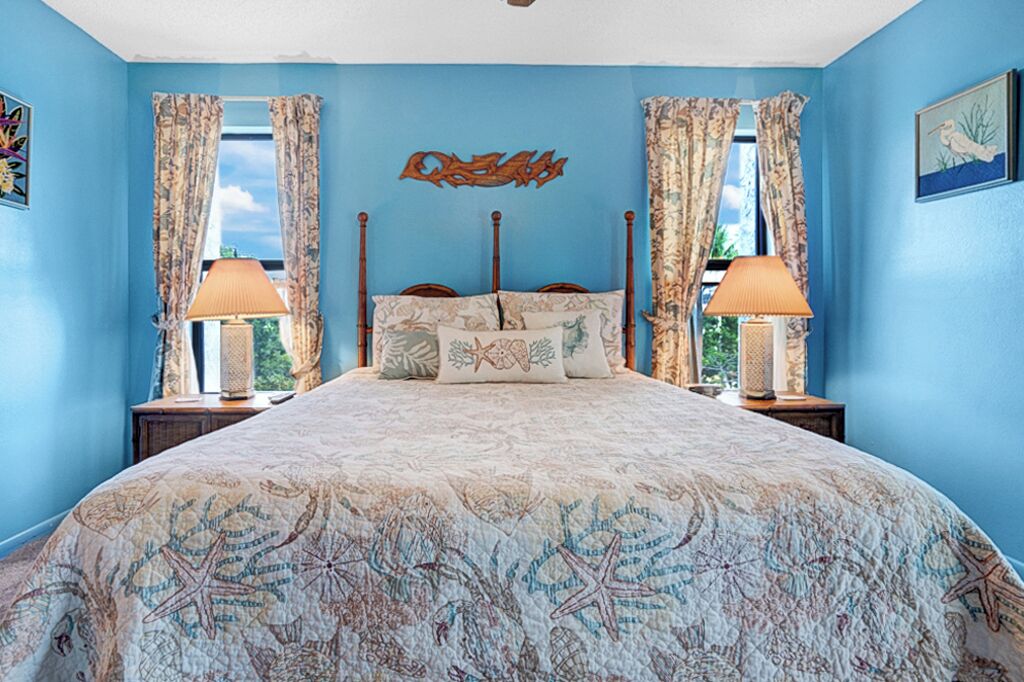 Une chambre à coucher avec un grand lit, deux tables de chevet, une tête de lit en bois et une fenêtre avec des rideaux.