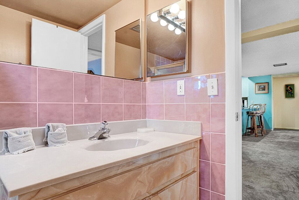 A bathroom with pink tiles, a sink, and a mirror with lights.