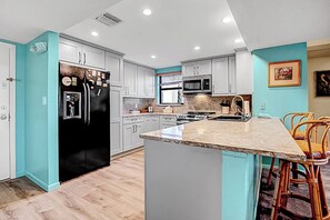 Une cuisine moderne avec des meubles blancs, un réfrigérateur noir, un four à micro-ondes et une cuisinière.
