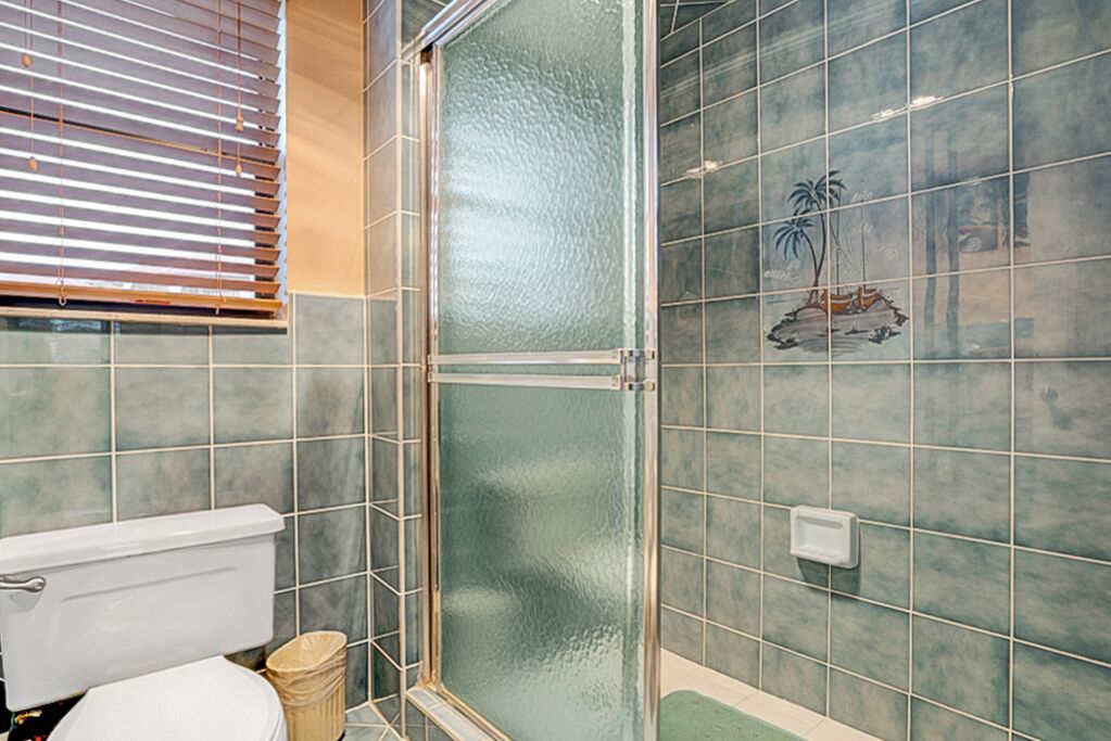 A bathroom with a toilet, a glass-enclosed shower, and tiled walls.