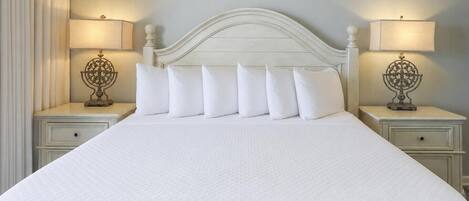 A bed with a white headboard and six pillows, flanked by two bedside tables with lamps and decorative metal stands.