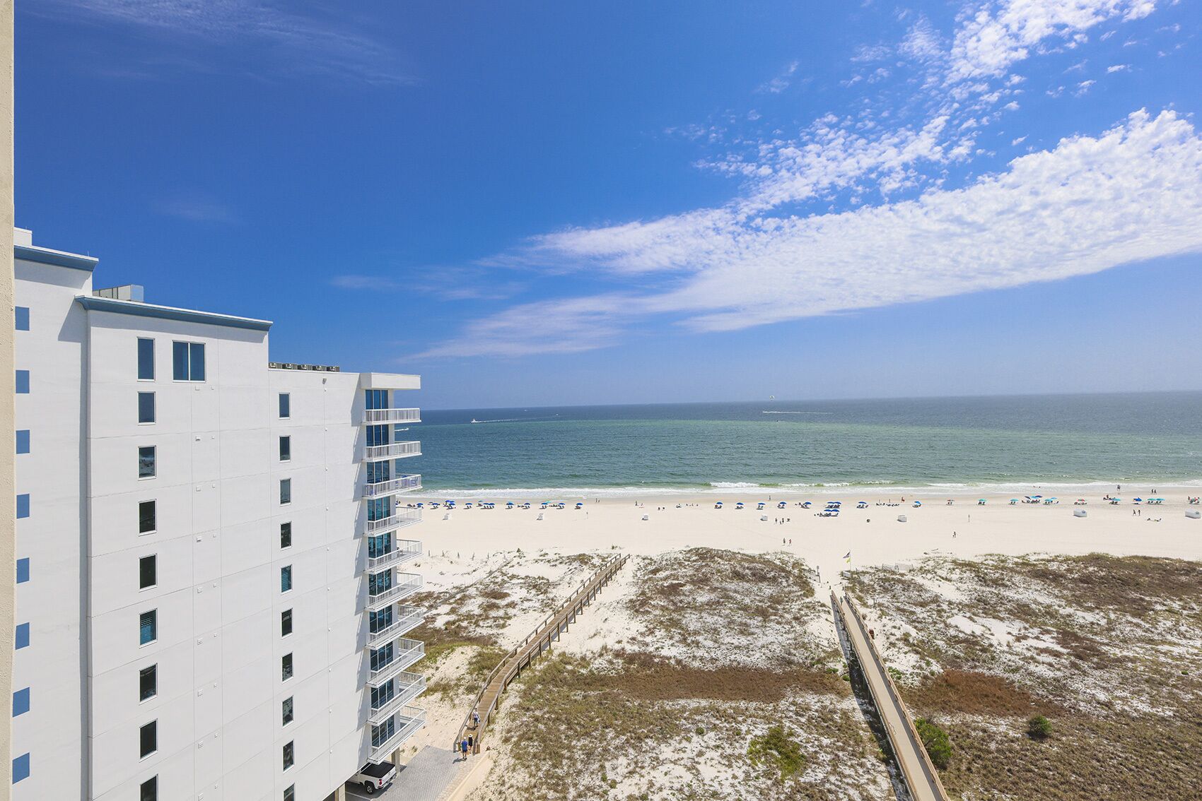 A beachfront hotel with a sandy beach, ocean view, and a clear sky.
