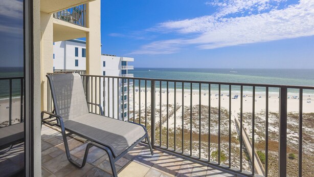 A balcony with a chair, overlooking a beach with a clear sky and a building in the background. - See why this condo is in High Demand! 3BR 2BA @ Phoenix 8! (Orange Beach)
