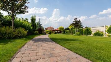 A paved pathway leading to a house with a red roof, surrounded by lush greenery and a clear sky.