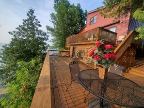 Eine Holzterrasse mit Gartenmöbeln, einer Treppe und einem roten Gebäude mit Fenstern.