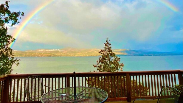 Een terras met tafel en stoelen met uitzicht op een waterpartij en een regenboog.