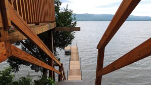 Een houten terras dat leidt naar een steiger boven het water, met bergen op de achtergrond.