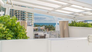 A rooftop terrace with a view of the ocean, a white pergola, and a seating area with a table and chairs.