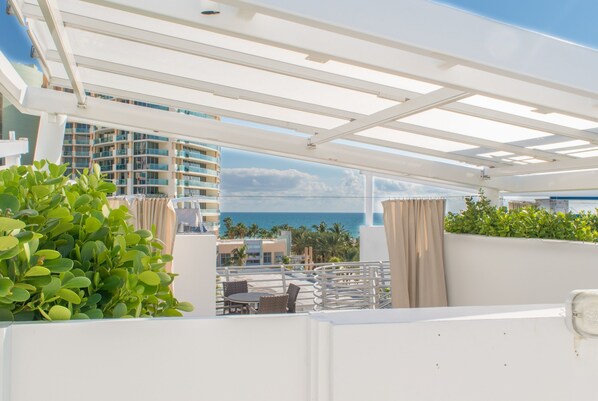 A rooftop terrace with a view of the ocean, a white pergola, and a seating area with a table and chairs. - Two Story Penthouse Suite with Hot Tub on Ocean Drive (Miami Beach)