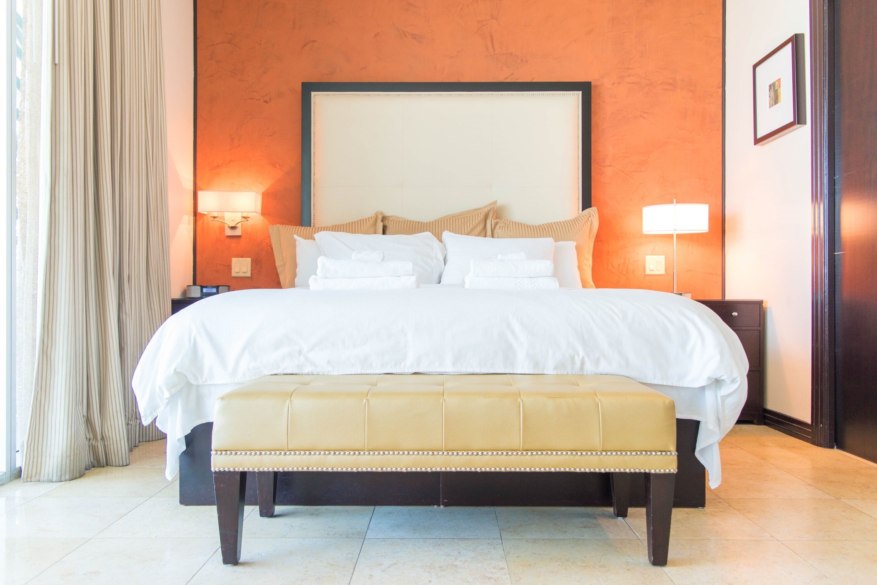 A hotel room with a large bed, two bedside lamps, a bench, and a nightstand.