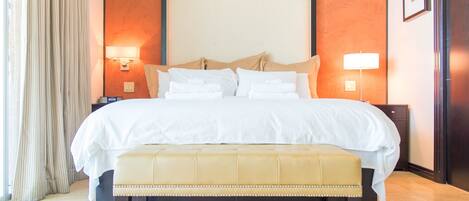 A hotel room with a large bed, two bedside lamps, a bench, and a nightstand.