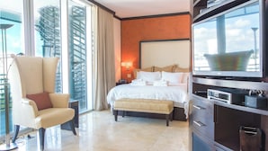 A hotel room with a bed, a TV, a chair, and a large window with a city view.