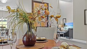 Uma mesa de jantar com um vaso de flores secas, uma televisão e vista para o exterior.