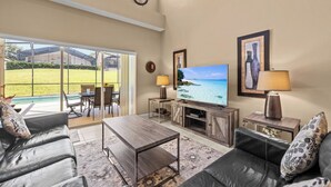 Uma sala de estar ampla com uma televisão grande, assentos confortáveis e vista para o exterior.