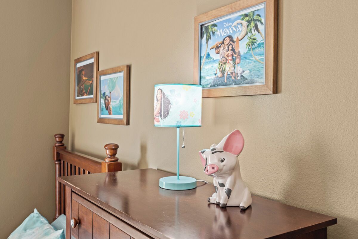 A wooden desk with a pig-shaped lamp, framed Disney movie posters, and a blue lamp on the wall.