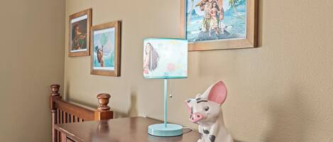 A wooden desk with a pig-shaped lamp, framed Disney movie posters, and a blue lamp on the wall.
