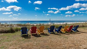 A row of colorful Adirondack chairs facing a beach with a clear sky.