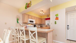 A compact kitchen with a central island, wooden cabinets, a microwave, and a dining area with white chairs.