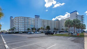 A large hotel with multiple floors, a parking lot, and palm trees.