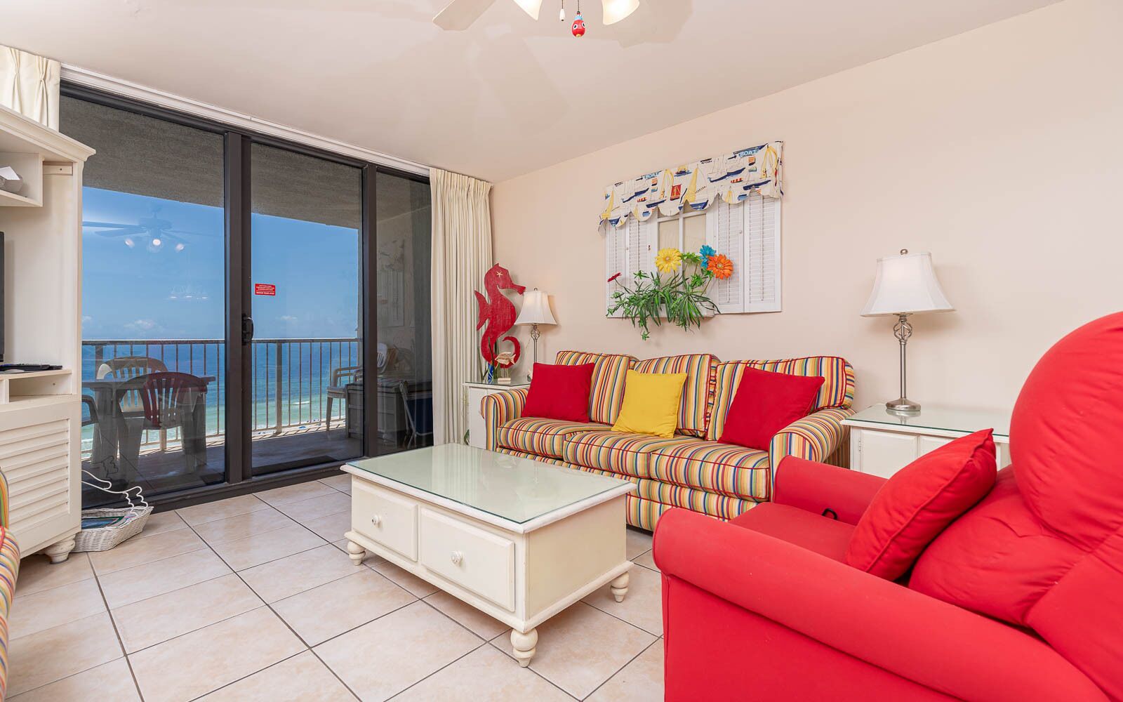 Un salon avec un canapé, une table basse et un fauteuil rouge. Il y a un balcon avec vue sur la mer.