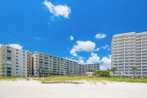 A beachfront hotel with multiple floors, balconies, and a sandy beach in the foreground.