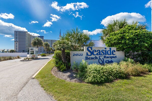A sign for Seaside Beach & Club with a number 24522, surrounded by greenery and palm trees. - 2 BR @ Seaside Beach & Racquet (Orange Beach)