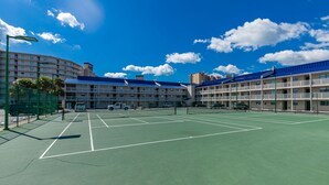 A tennis court with a net in the middle, surrounded by a fence. There are multiple tennis courts visible.