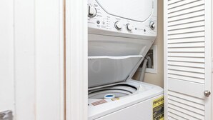 A front view of a laundry room with a stacked washer and dryer, control panel, and a door with a louvered design.