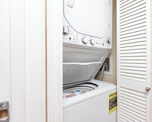 A front view of a laundry room with a stacked washer and dryer, control panel, and a door with a louvered design. - 2 BR @ Seaside Beach & Racquet (Orange Beach)