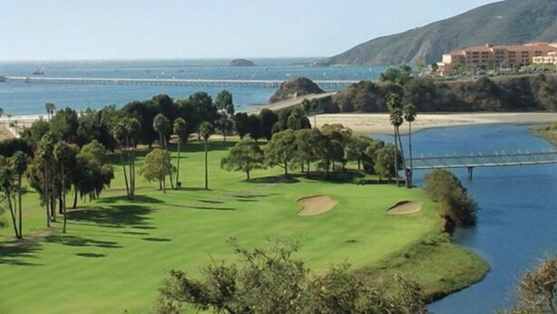 Un parcours de golf avec un plan d’eau, des arbres et un bâtiment situé au loin.
