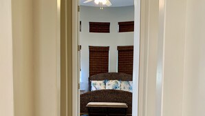 Un escalier menant à une chambre à coucher équipée d’un lit, d’un ventilateur de plafond et de deux fenêtres avec des stores.