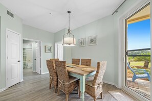A dining area with a table and chairs, a hanging light fixture, and a view through a glass door. - 105E 2Bed/2Bath Beautiful Gulf View (Gulf Shores)