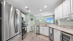 A modern kitchen with stainless steel appliances, white cabinetry, and a view to the outside. - 105E 2Bed/2Bath Beautiful Gulf View (Gulf Shores)