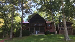 Une cabane en rondins à deux étages, dotée d’un balcon, entourée d’arbres et bordée d’un chemin rouge.