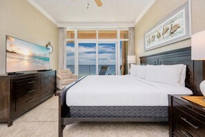 A hotel room with a bed, a TV, a chair, a large window with a view, and a painting on the wall.